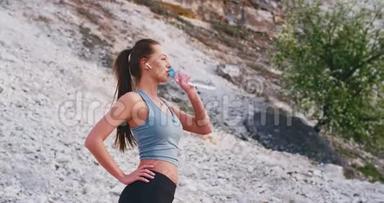 美丽的女人在大自然<strong>辛苦</strong>锻炼了一天后，一边听音乐一边喝着塑料瓶里的水